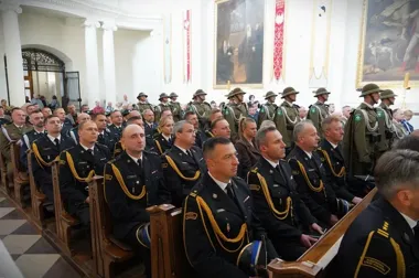 Funkcjonariusze służb mundurowych w galowych mundurach uczestniczą w uroczystości w kościele, w tle stoją żołnierze w historycznych hełmach.